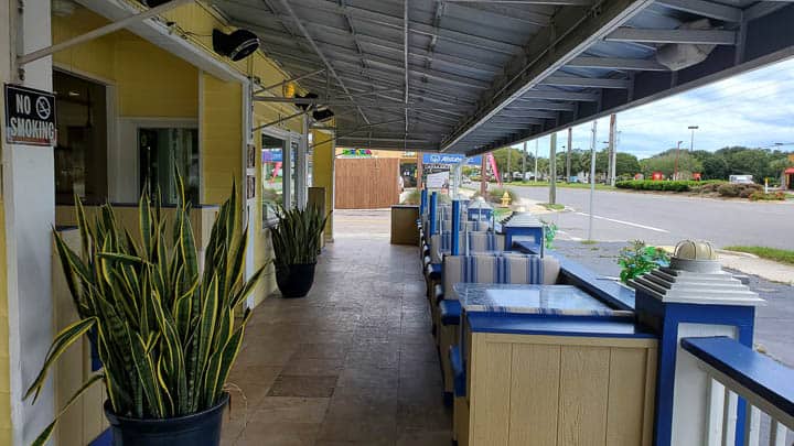 Outdoor seating at Beach Diner in Atlantic Beach, Florida showing cozy outdoor booths along a narrow covered outdoor patio with a plant in the foreground and the main doors leading inside to the left.