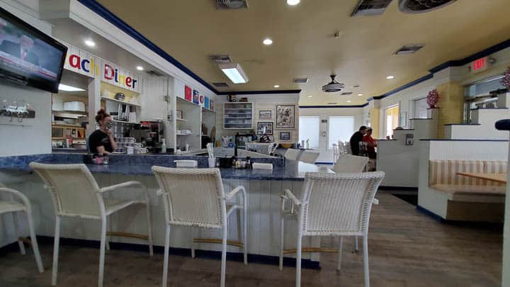 Counter seating area in Beach Diner at Atlantic Beach, Florida showing beach style chairs, blue countertop, and serving area with a masked server and customers in the background.